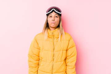 Young caucasian woman wearing a ski clothes in a pink background blows cheeks, has tired expression. Facial expression concept.