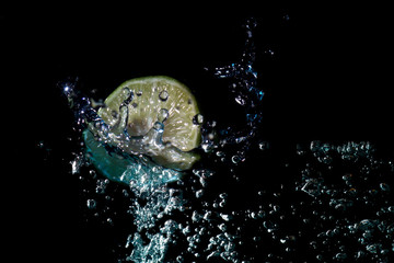 Slice of fresh green lemon into the water until the water spreads, creating beautiful bubbles in a black background.