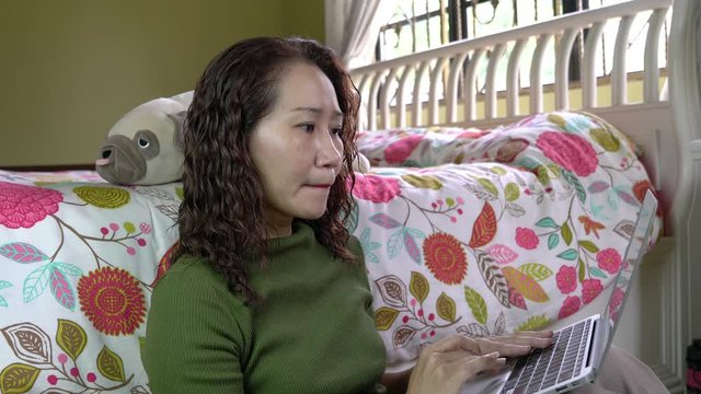Work from home concept. Asian Chinese woman typing on her laptop in her bedroom.