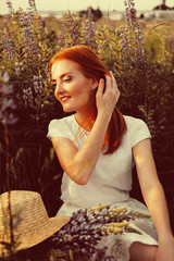 Feminine natural beauty. Young adult redhead woman sitting in the field of flowers.