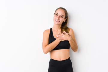 Young caucasian fitness woman posing in a white background has friendly expression, pressing palm to chest. Love concept.