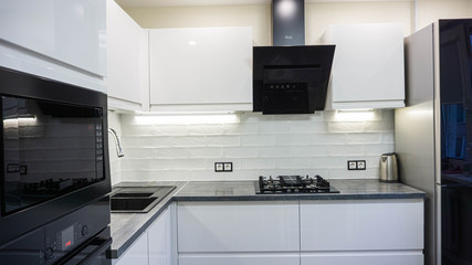 interior of a modern white kitchen with black appliances, stove oven, extractor hood and refrigerator.