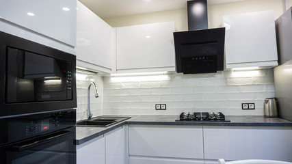 interior of a modern white kitchen with black appliances, stove oven, extractor hood and refrigerator.