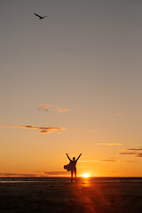 Unrecognizable woman with positive arms raised on sunset background. Positive emotions on a walk on the seashore at dawn. A woman enjoys the sun.