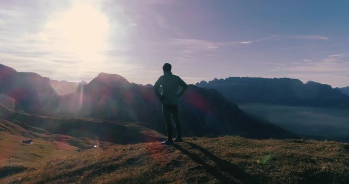 Aerial View. Young man in sport trail clothes stretching on Seceda mountain peak at sunrise. Puez Odle, Trentino, Dolomites, Italy.