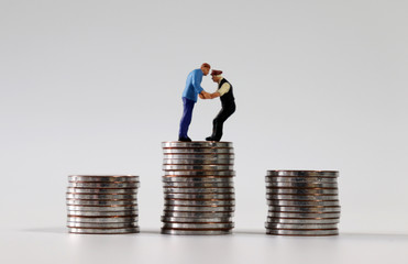 Two miniature men fighting on a pile of coins.