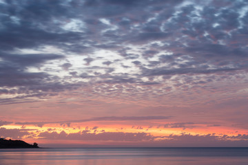 Naklejka na ściany i meble Stunningly vibrant sunset over the ocean with land