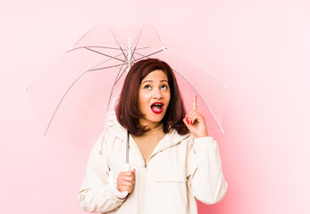 Middle age latin woman wearing an umbrella isolated pointing upside with opened mouth.