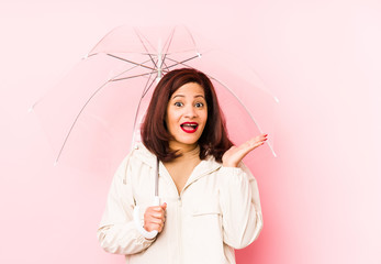 Middle age latin woman wearing an umbrella isolated surprised and shocked.