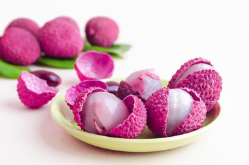 peeled ripe exotic tropical lychee fruit, in shell, with seeds, green leaves on white background close up, soft focus