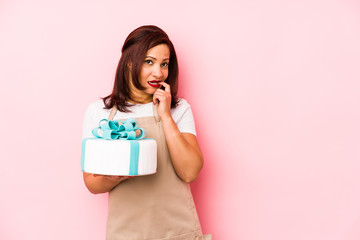 Middle age latin woman holding a cake isolated on a pink background relaxed thinking about something looking at a copy space.