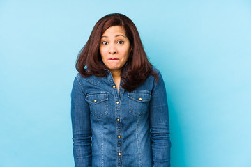 Middle age latin woman isolated on a blue background shrugs shoulders and open eyes confused.