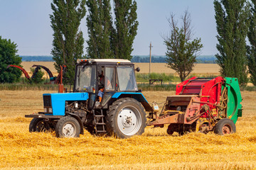 tractor makes big straw roll on yellow field at summer day