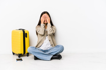 Young chinese traveler woman sitting holding a boarding passes covers eyes with hands, smiles broadly waiting for a surprise.