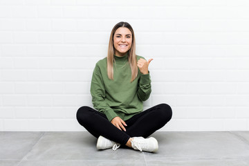 Young caucasian woman sitting on the floor smiling and raising thumb up