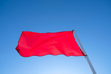 A red flag in the wind isolated on bright blue sky background.