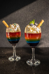 Colored rainbow jelly, layered jelly in a glass with whipped cream and blueberries on a dark background