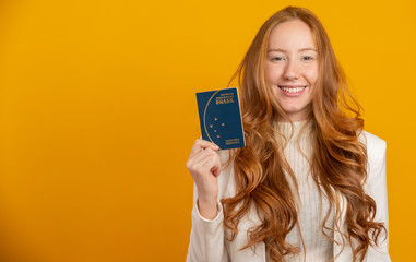 Beautiful redhead curly-haired girl in travel. Next trip. Girl holding Brazilian passport. On yellow.