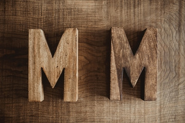 Two M letters made of wood. Name and surname, family name initials. Carpentry business background.