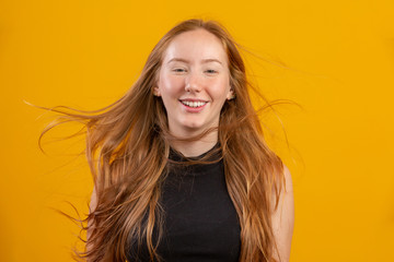 Fototapeta premium Portrait of beautiful cheerful redhead girl with flying hair smiling laughing looking at camera over yellow background.