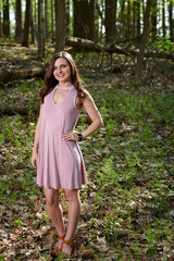 Gorgeous young Caucasian woman in pink cocktail dress stands in summer forest setting