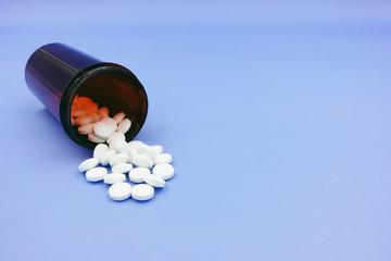 Close up, top view of pill container and circle pill spill out of the bottle, isolated on blue background. For medical, pharmaceutical and science theme. Selective focus with copy space.