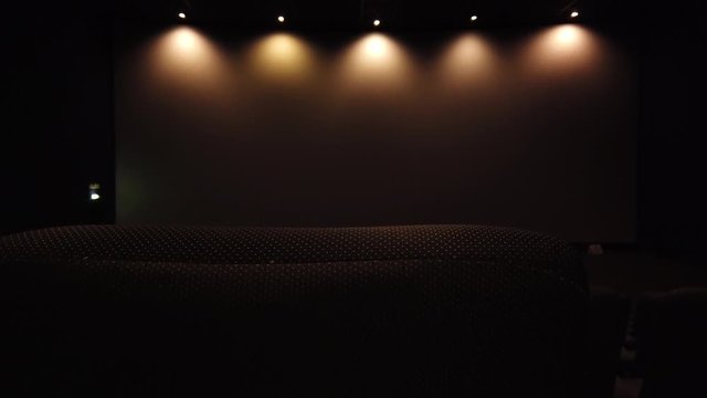 A shot revealing from behind a seat a empty movie teather. the lights go out at the end of the shot.