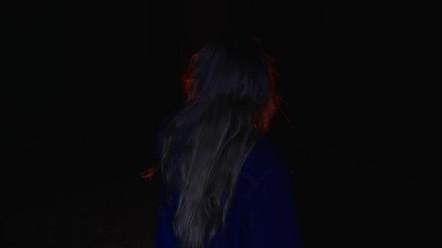 Back view of girl holding kerosene oil lamp and walking in dark forest at night. Rear view of teenage girl holding vintage lantern and walking in mysterious darkness at night time