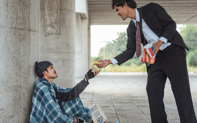 Two parts. Kind-hearted businessman dividing his big meat burger in two parts while giving one of...