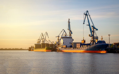 Cargo ship being loaded up by a crane with containers at port of Riga, Europe, sunset, evening...