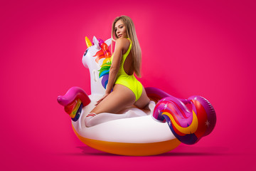 Beautiful slim woman in a summer clothes, having fun and enjoying life on a white inflatable unicorn on a pink isolated background. Concept summer mood, relaxation and beauty. © Виталий Сова