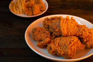Fried chicken and French fries in white dish on wooden table with orange light.