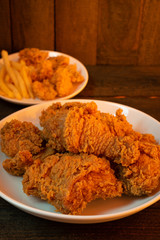 Fried chicken and French fries in white dish on wooden table with orange light.