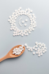 White pills in a wooden spoon on a pastel blue background. Flat lay, top view, layout, template, copy space. Pharmacy and medical concept