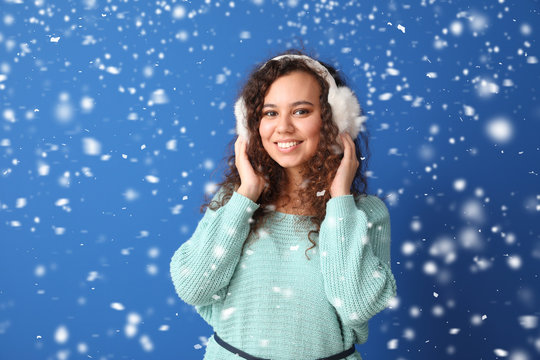 Young African-American woman in warm sweater and falling snow on color background