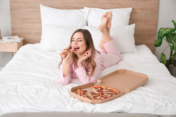 Morning of beautiful young woman eating tasty pizza in bedroom