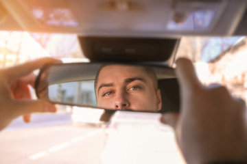 Driver adjusting rear view mirror in car