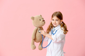 Cute little doctor with toy on color background