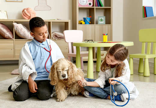 Cute Little Children Dressed As Doctors Playing With Dog At Home