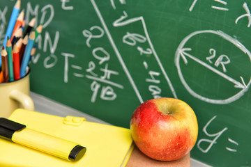 Set of school supplies and apple on table near blackboard