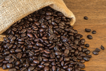 Roasted Coffee Beans spilled from Jute Bag on wooden boards