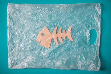 Concept of ocean plastic pollution. Fish skeleton made of cardboard in plastic bag on blue background.