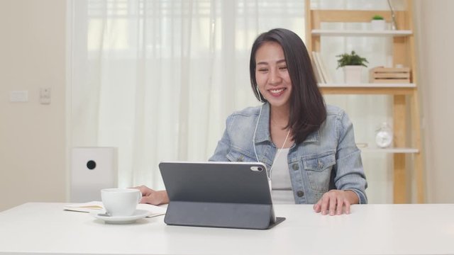 Slow motion - Freelance business women using tablet working call video conference with customer at living room. Happy young Asian girl relax sitting on desk do job in internet. Work from home concept.