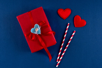 Red gift box with heart and bow paper straw on classic blue 2020 color background. Valentines day 14 february packaging concept. Flat lay, copy space, top view.