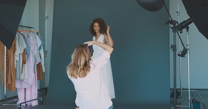 Young professional studio photographer taking photos of an african american fashion model in front of a blue seamless with multiple flashes, high end fashion photoshoot behind the scenes