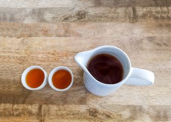 A jar of hot tea and two cups on brown wooden table for drinking time, top view image
