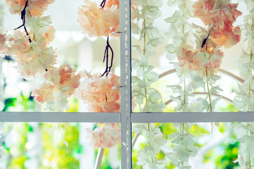 Beautiful artificial flowers hung on glass windows to decorate for a garden party. View from the window on the glass.