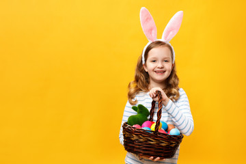 Cheerful happy child in bunny ears holds a basket with Easter eggs. Portrait of a cute beautiful...