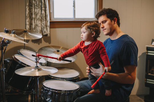 Father teaching baby boy to play drums. Parent with toddler child having fun and spending time together. Dad with kid playing music. Family hobby activity and leisure time.