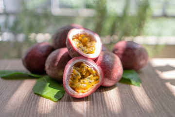 A group of purple skin passionfruit plant, sliced and round fruits under sunlight morning on wooden table, blurred background